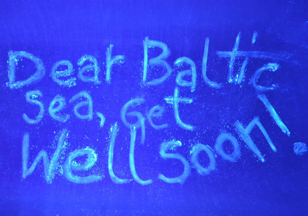 Uzraksts Dear Baltic Sea, Get Well Soon zilā UV gaismā