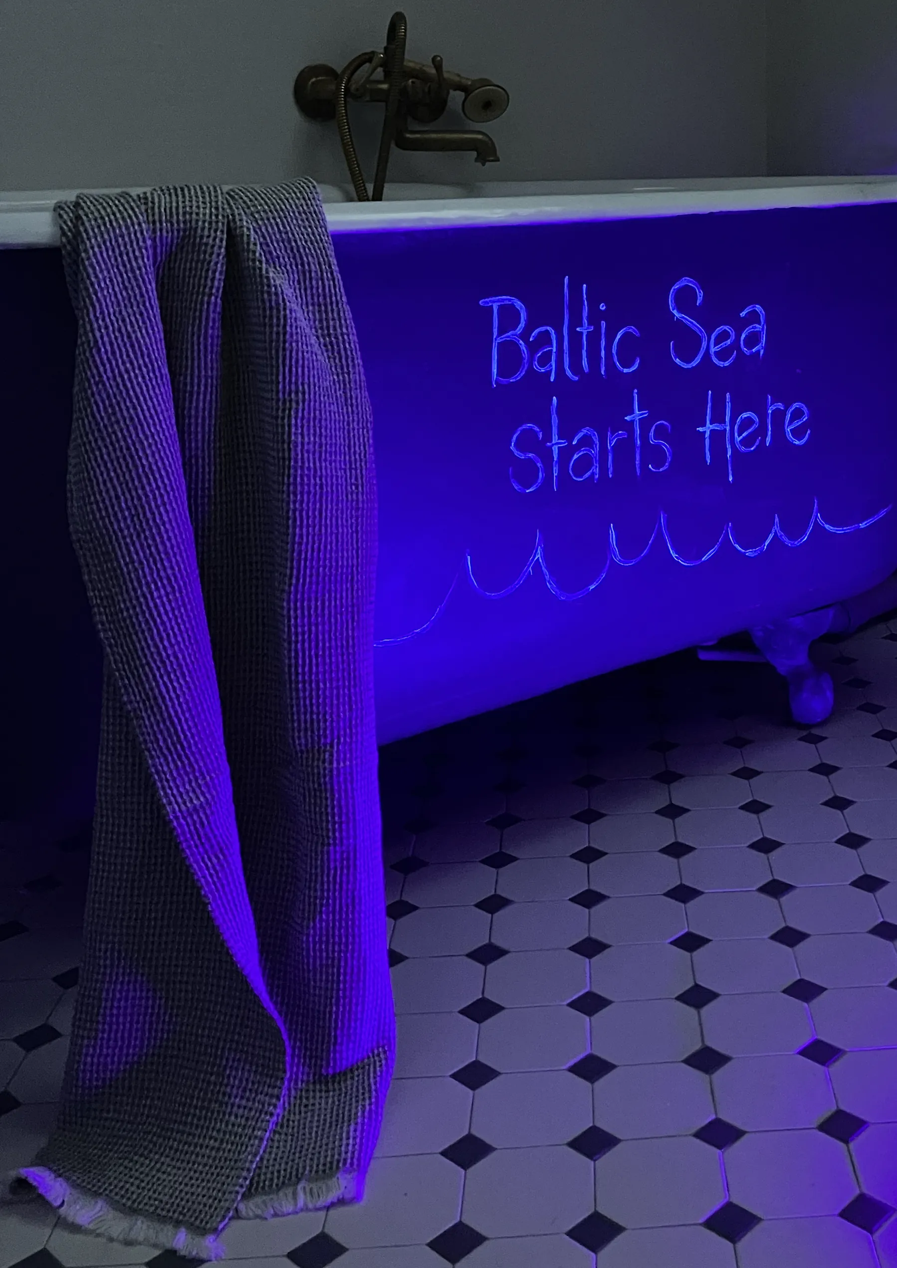 Pie vannas malas pakārts dvielis un UV gaismā izgaismots uzraksts Baltic Sea Starts Here