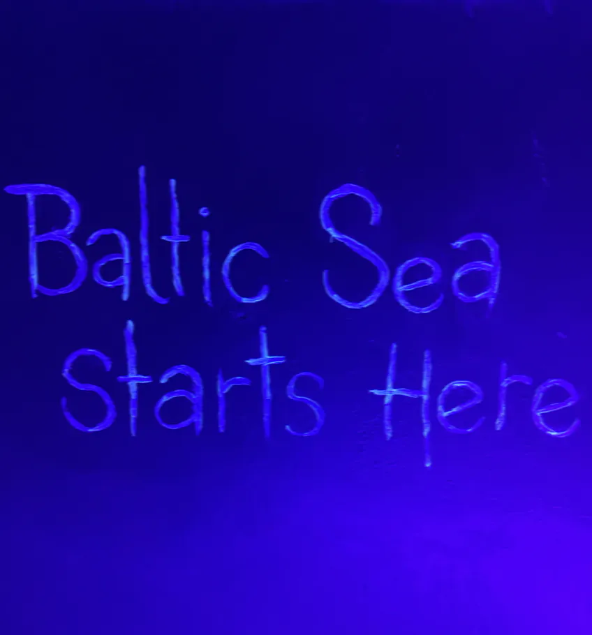 Uzraksts Baltic Sea Starts Here uz violeti izgaismotas sienas